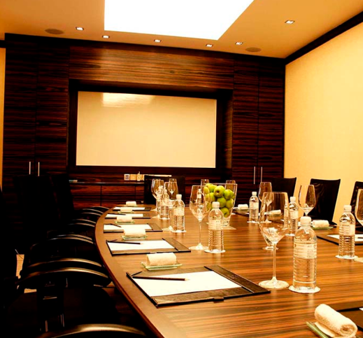 image of a board room with writing materials on a board meeting table with chairs on all sides 